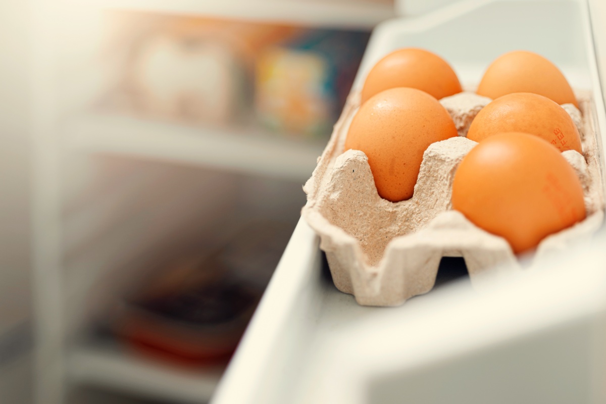 Ein Eierkarton gefüllt mit Eiern im offenen Kühlschrank.