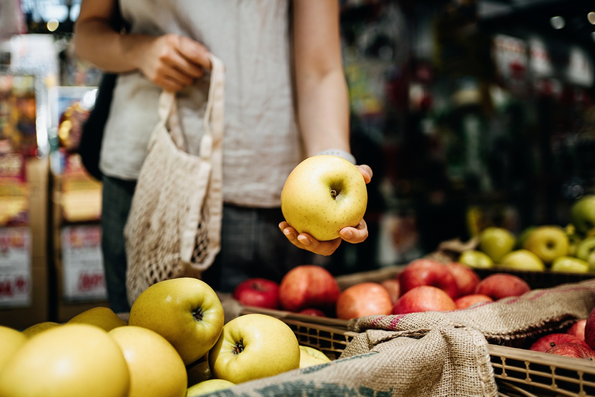 Eine Frau greift nach unverpackten Äpfeln im Geschäft.