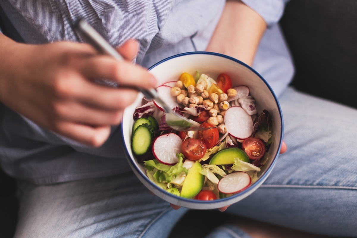 Person hält eine Schüssel mit frischem Gemüsesalat und isst mit einer Gabel.