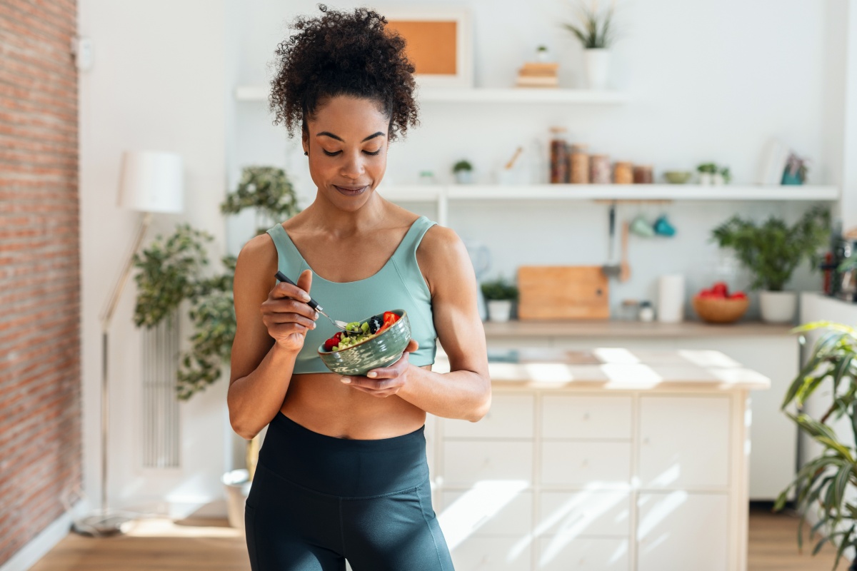 Frau in Sportkleidung isst eine selbstgemachte Bowl in einer modernen Küche nach dem Training.