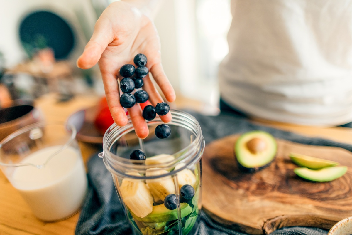 Eine Hand wirft ein paar Heidelbeeren in einen Mixer voller Obst.
