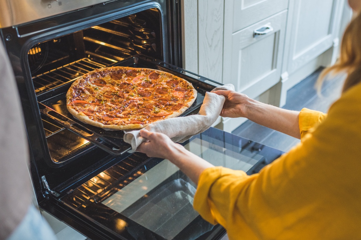 Eine fertig gebackene Pizza wird von einer Frau aus dem Ofen geholt.