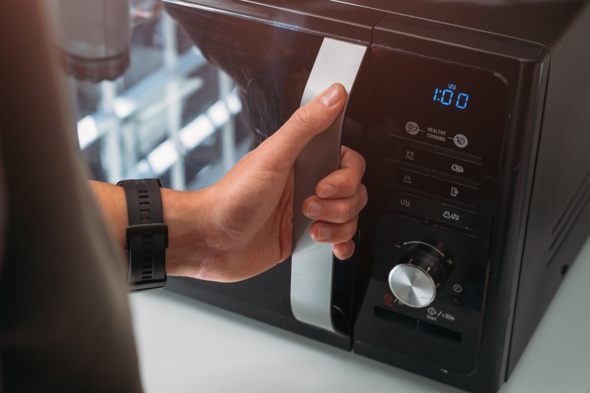 Eine Hand öffnet die Tür einer Mirkowelle.