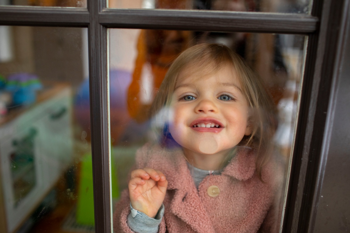 Ein kleines Mädchen presst ihr Gesicht gegen eine frisch geputzte Fensterscheibe.