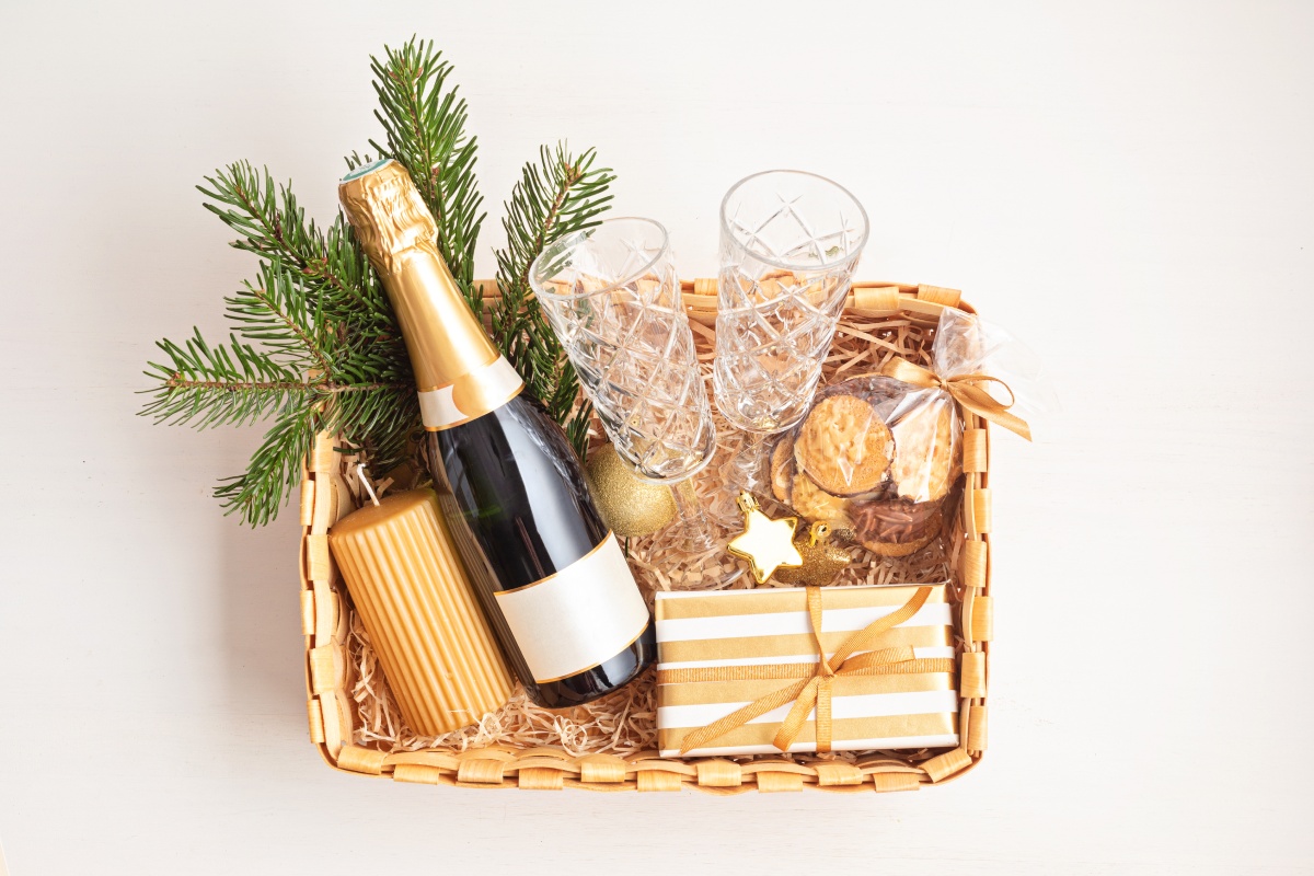 Geschenkkorb mit Sekt, Tannenzweigen, Keksen, Gläsern und goldenen Dekorationen.