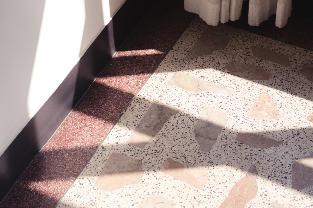 Fußboden im Terrazo-Stil, Schatten fallen auf den Boden und die Wand, unterer Teil eines Vorhangs ist zu erkennen.