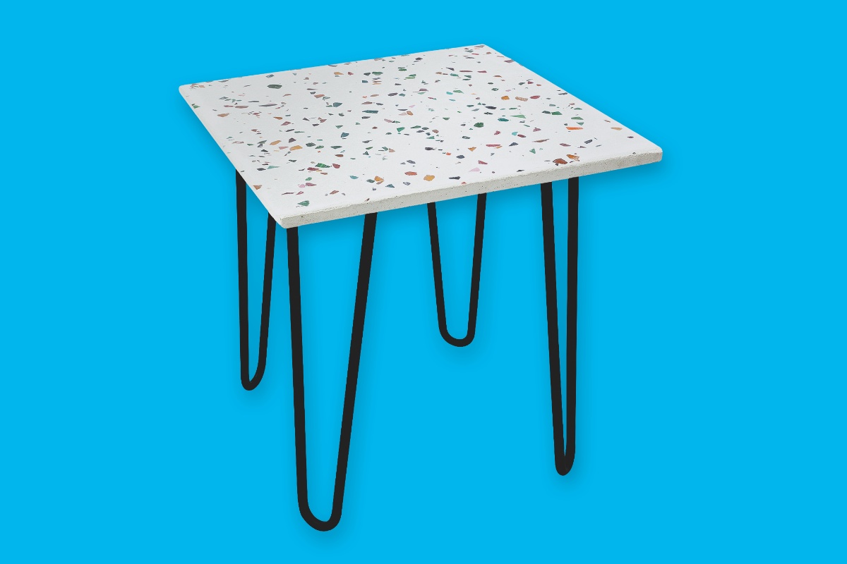 Viereckiger Terrazzo-Tisch mit gebogenen Tischbeinen vor blauem Hintergrund.