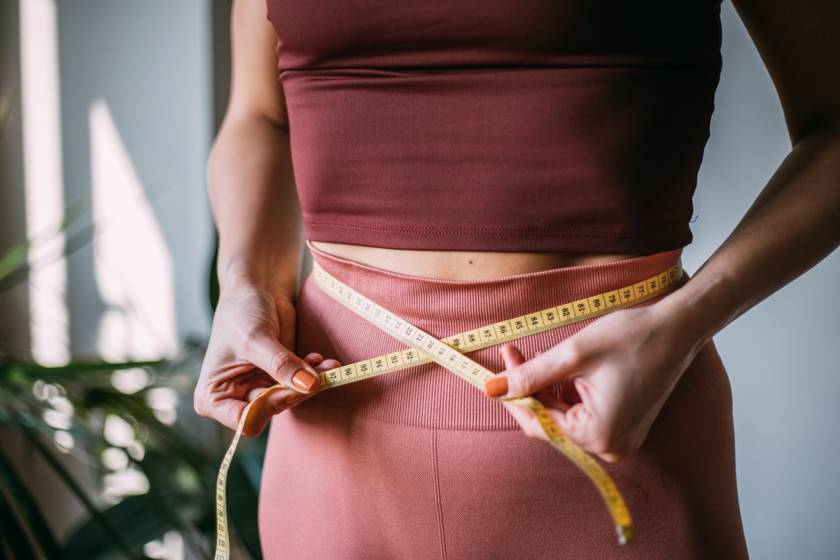 Frau in Sportkleidung misst mit einem Maßband ihren Taillenumfang.