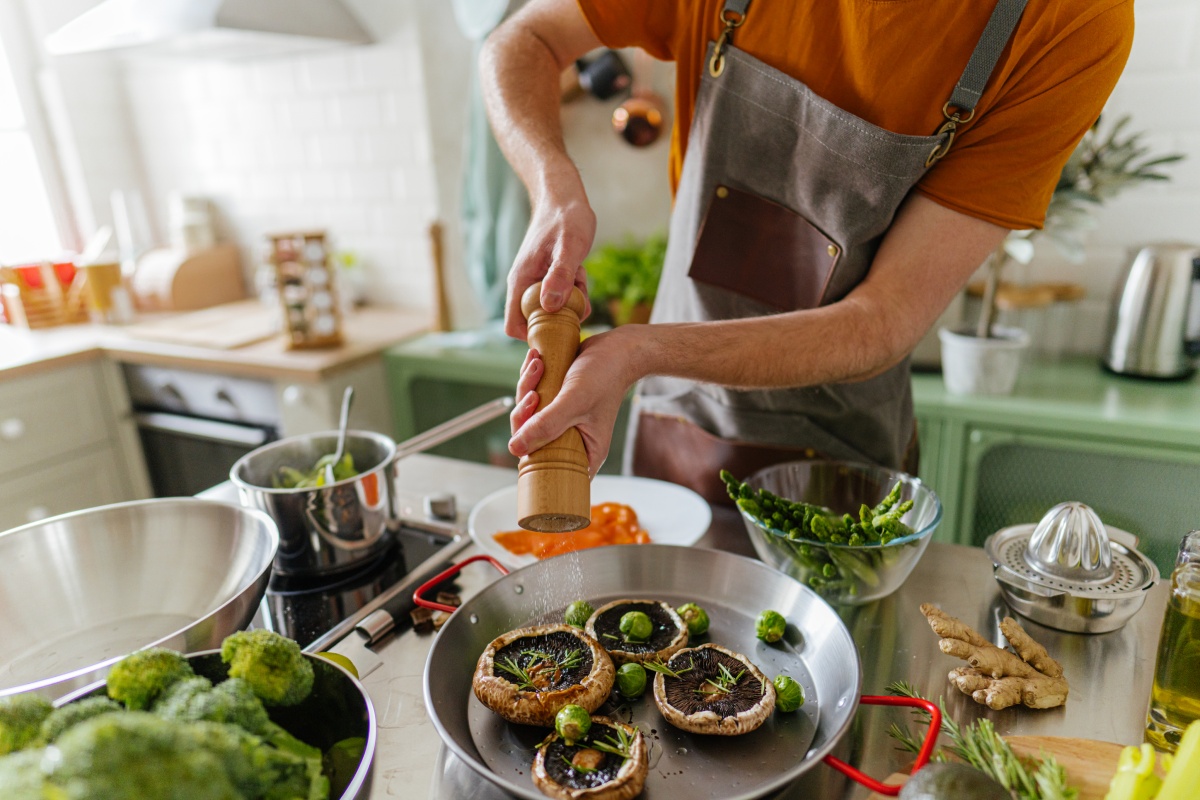 Person würzt Portobello-Pilze und Rosenkohl in einer Pfanne über dem Herd.