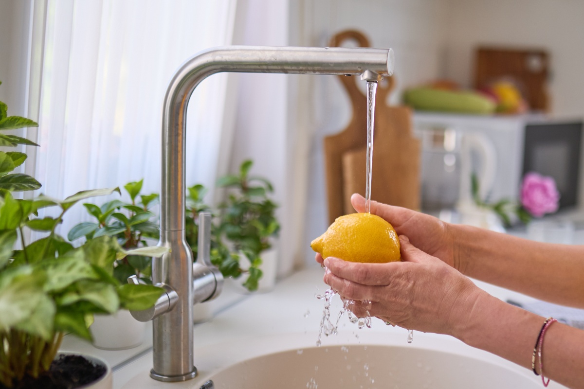 Person wäscht eine Zitrone unter fließendem Wasserhahn.