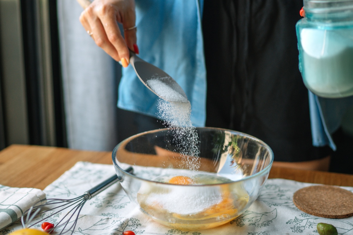 Person gibt Zucker in eine Schüssel mit Eiern, als Vorbereitung zum Backen.