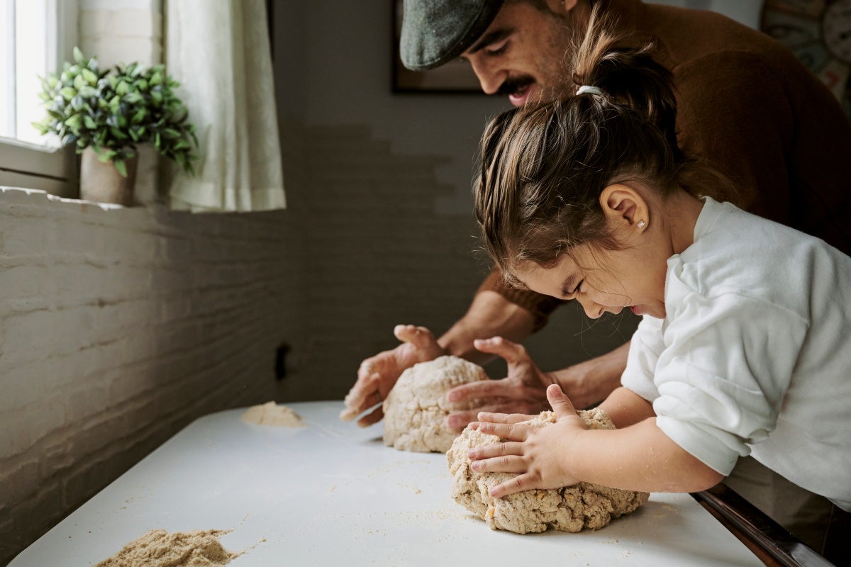 Vater und Tochter kneten gemeinsam Teig auf einem Tisch.