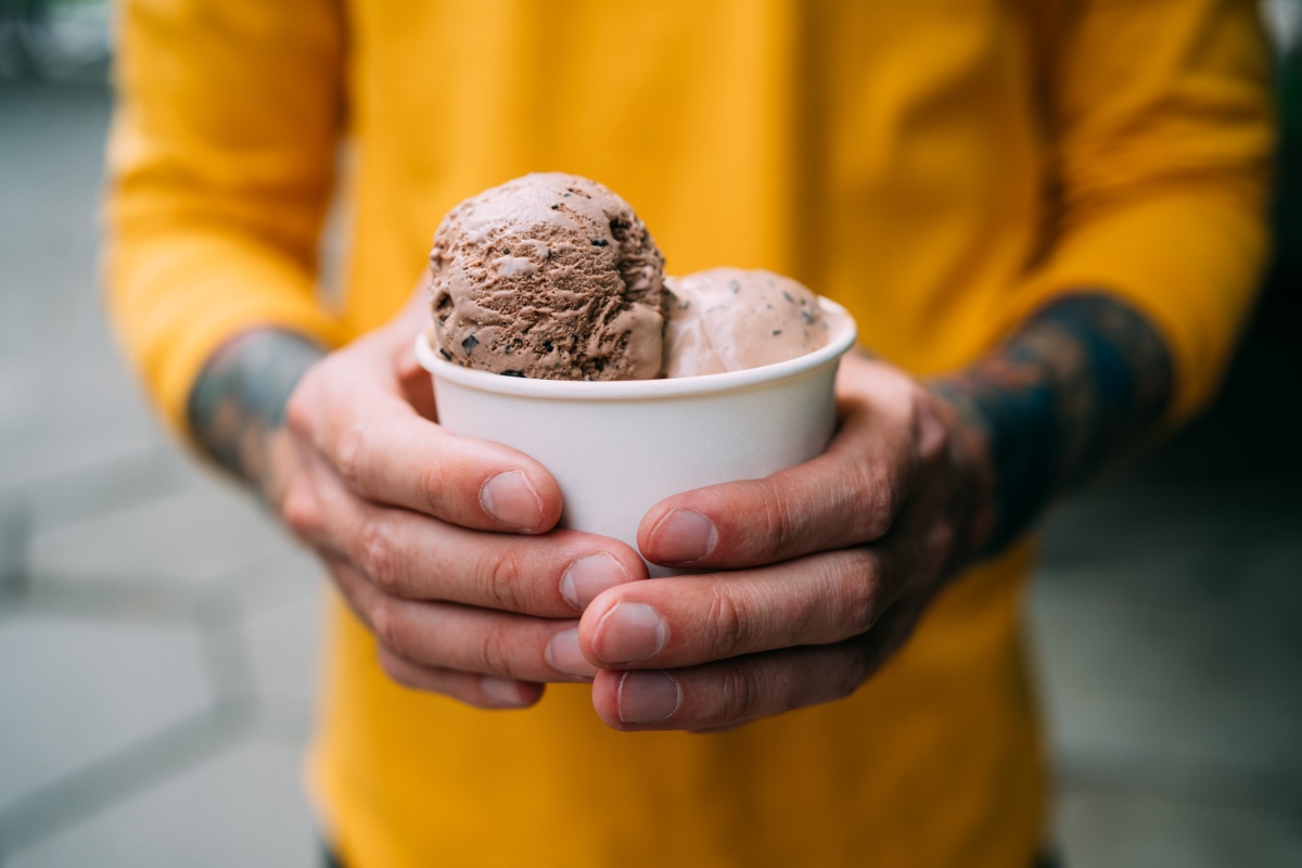 Eine Person in einem gelben Shirt hält einen Eisbecher in der Hand.