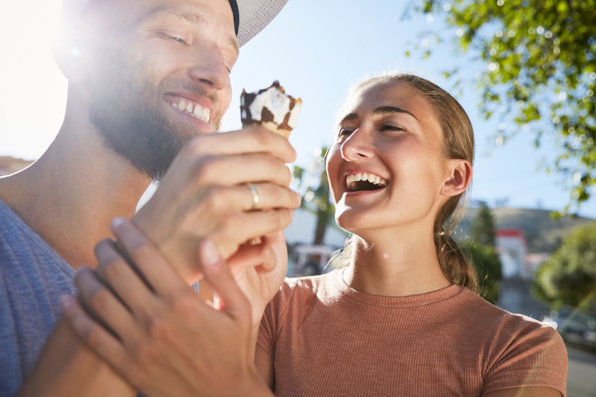 Lachendes Paar teilt sich ein Hörnchen-Eis bei Sonnenschein.