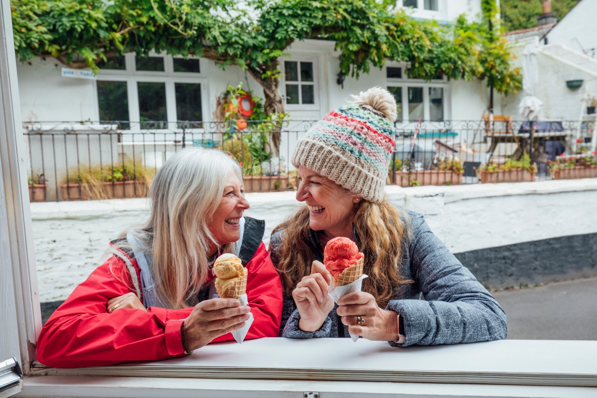 Zwei fröhliche Frauen genießen ein Eis in der Waffel bei kühleren Temperaturen.