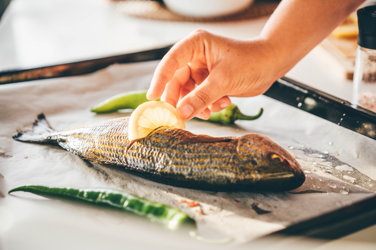 Eine Person steckt eine Zitronenscheibe in eine gebackene Forelle.