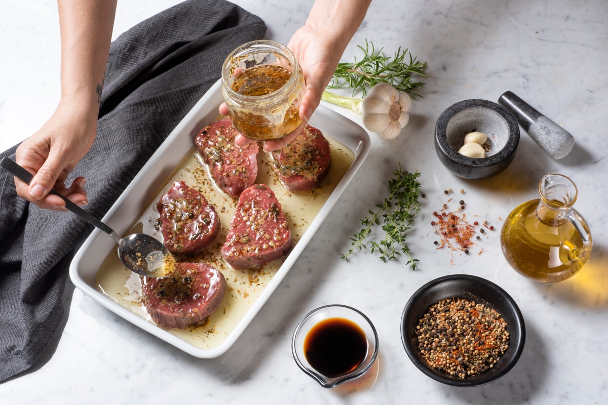 Steaks werden in einer Auflaufform mit Marinade beträufelt.
