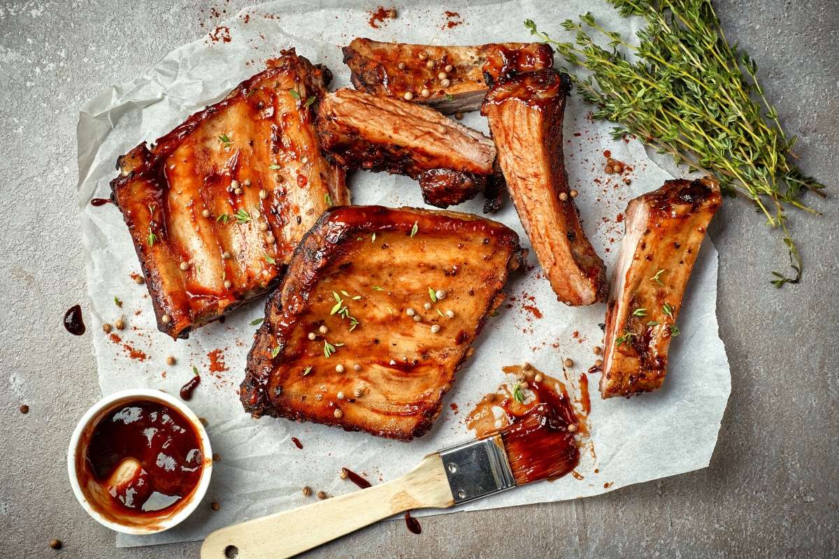 Marinierte Rippchen mit Thymianzweigen, Pinsel und der Marinade auf einem Stück Backpapier.