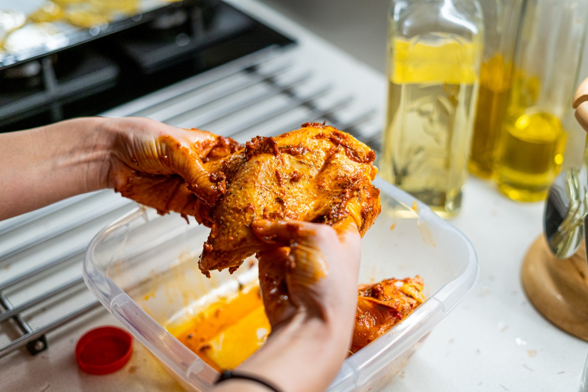 Eine Person mariniert eine Hühnerbrust mit den Händen.
