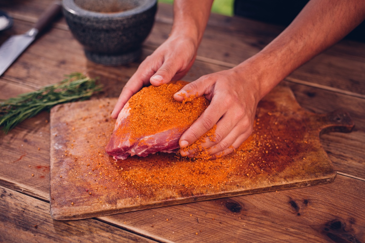 Eine Person reibt ein Stück Fleisch mit der Trockenmarinade Rub Magic Dust ein.