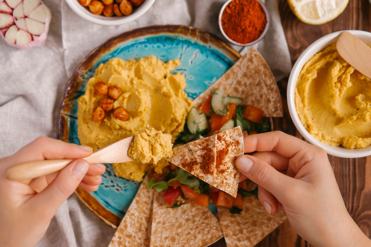 Mehrere Ecken Pitabrot liegen auf einem Teller mit griechischem Salat. Ein Stück Pita wird mit einer griechischen Paste bestrichen.