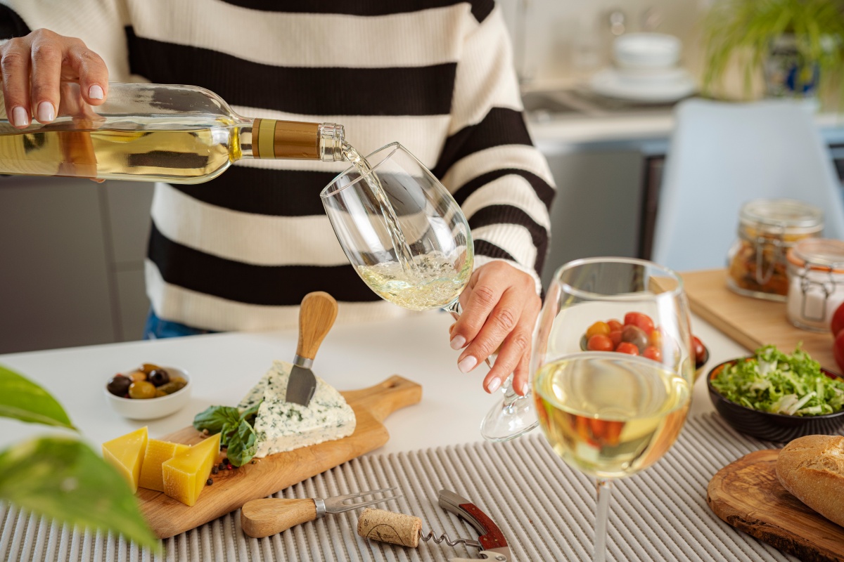 Eine Frau schenkt zu einer Käseplatte Weißwein in Gläser ein.