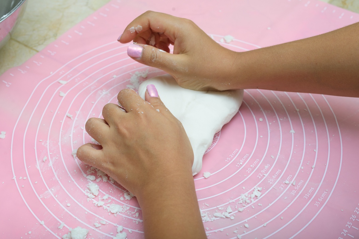 Jemand knetet mit den Händen einen weißen Teig auf einer rosa Backunterlage mit kreisförmigen Markierungen und Mehlresten.