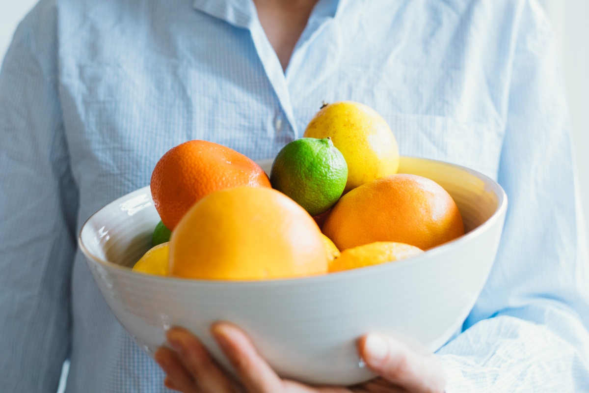 Person hält eine Schüssel mit bunten Zitrusfrüchten, darunter Orangen, Zitronen und Limetten.
