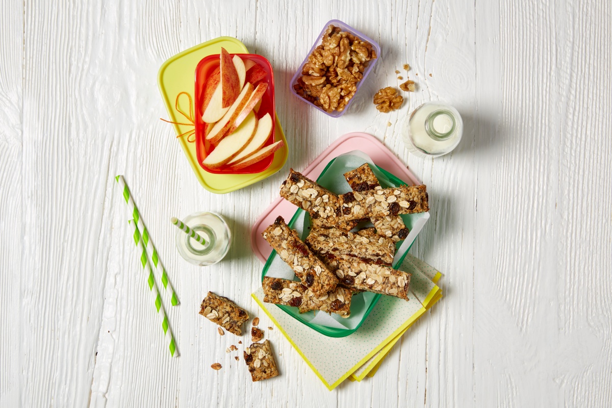 Leckere Zutaten für das Pausenbrot, wie Apfel, Müsliriegel und Nüsse liegen auf dem Tisch.