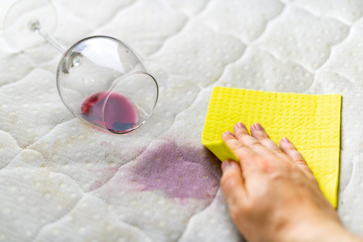 Eine Person tupft mit einem gelben Schwamm auf einen Rotweinfleck, der gerade einen hellen Stoff verfärbt