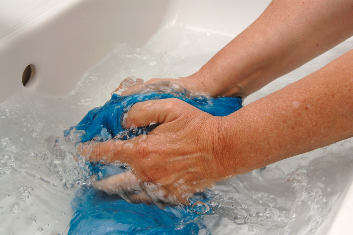 Eine Person wäscht ein blaues Kleidungsstück aus Wolle in einem Waschbecken mit klarem Wasser