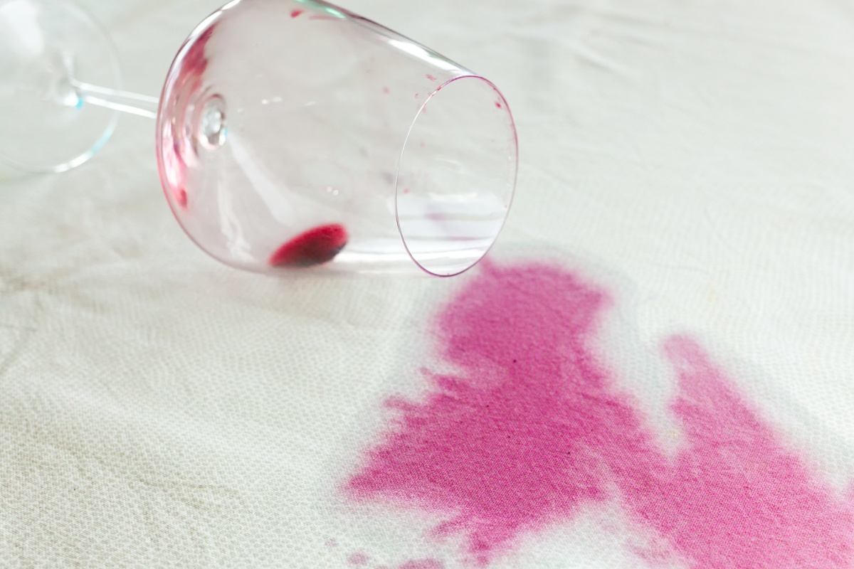 Ein umgefallenes Glas Rotwein hinterlässt einen Fleck auf einem weißen Stoff.