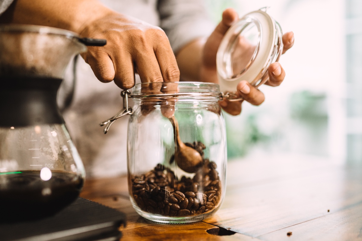 Eine Person nimmt geröstete Kaffeebohnen aus einem Einmachglas.