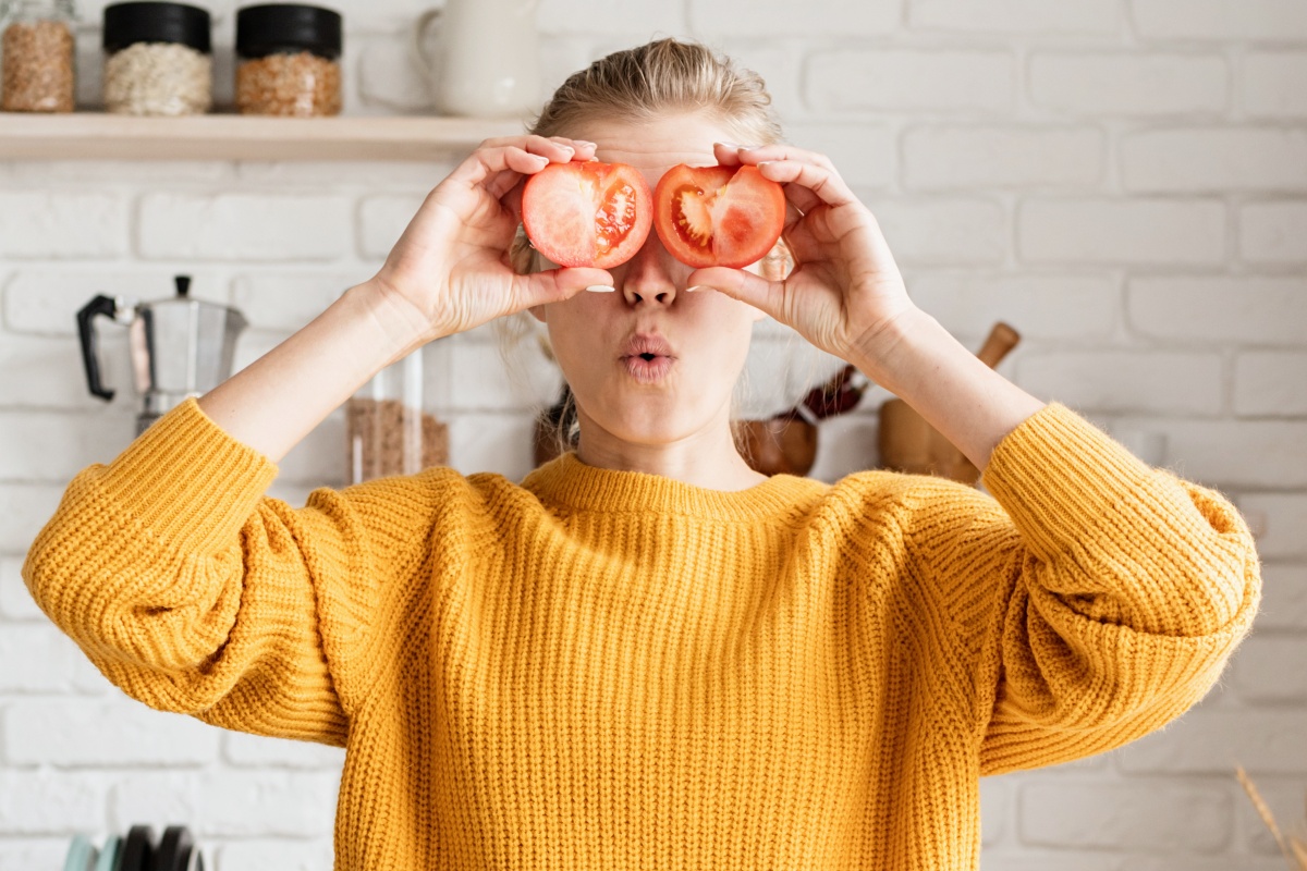 Junge Frau mit gelben Woll-Pullover hält sich zwei Tomatenhälften vor die Augen.