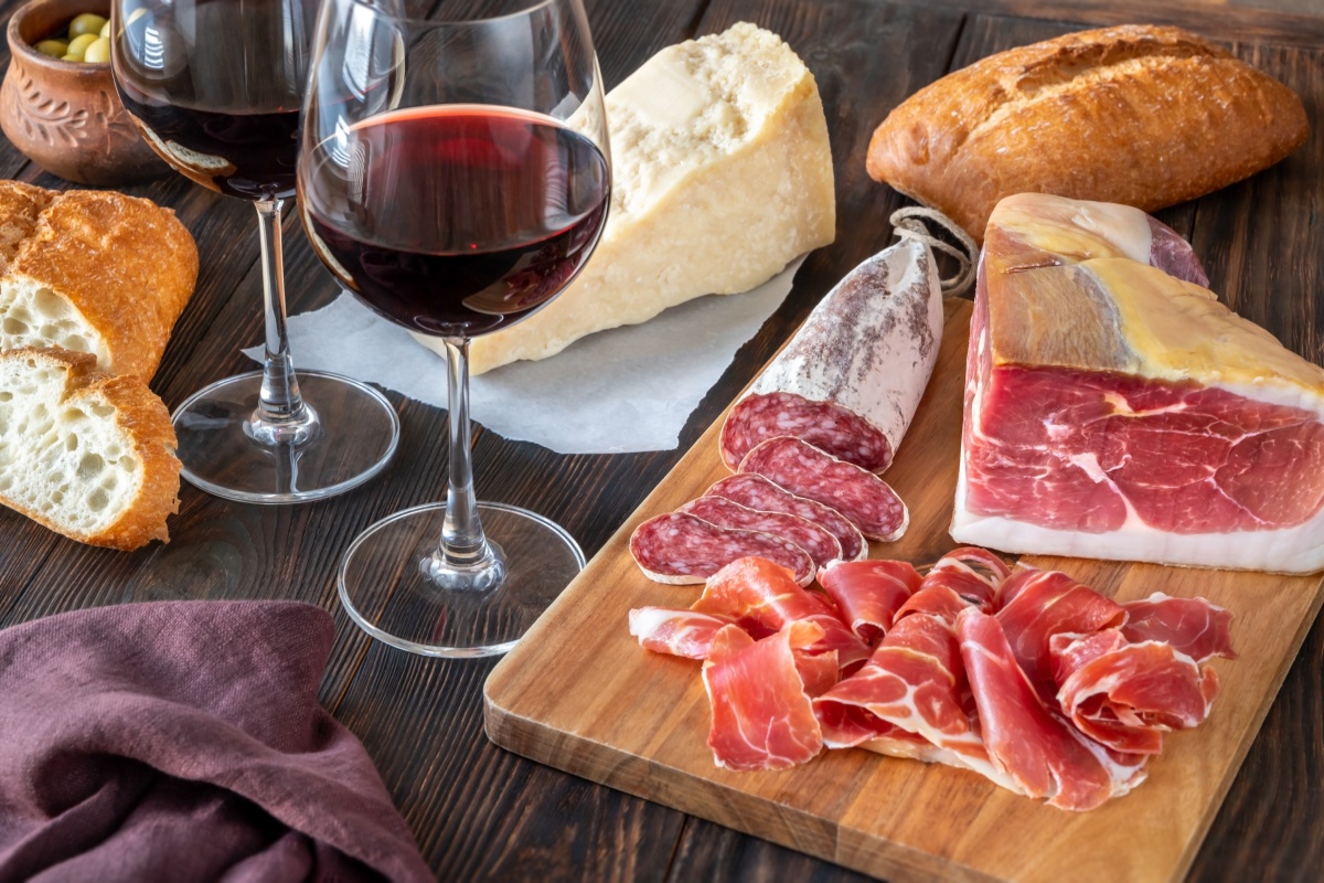 Rotwein im Glas, Schinken, Salami, Käse und Brot auf einem Holztisch, serviert für eine Pfälzer Brotzeit.