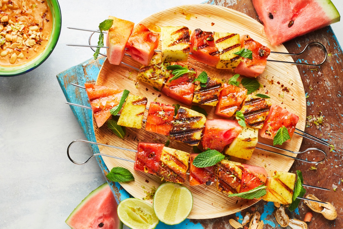 Fertige Grillspieße mit Wassermelone und Räuchertofu liegen auf einem Holzteller, dazu steht ein feiner Dip bereit