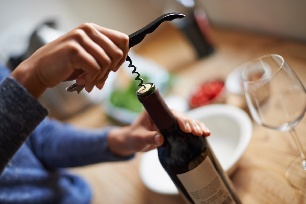 Eine Person öffnet eine Flasche Rotwein, die einen Korken hat.
