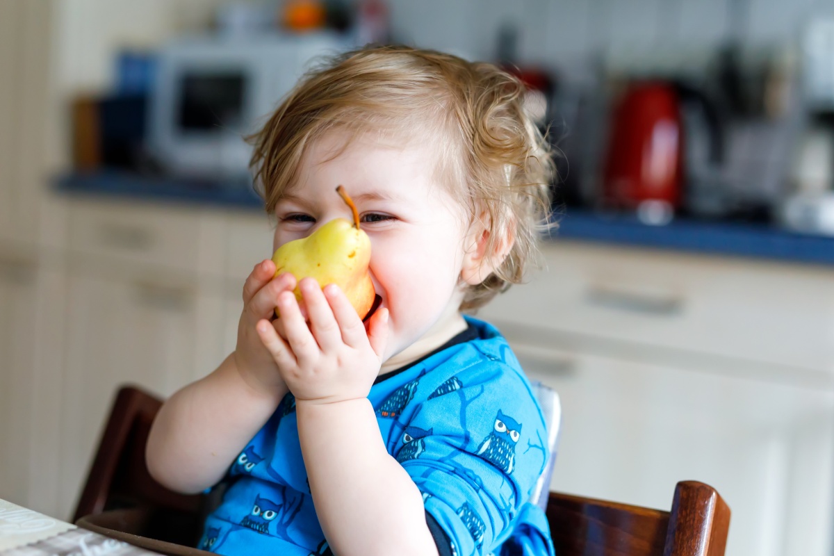 Ein Kleinkind beißt herzhaft in eine frische Birne.