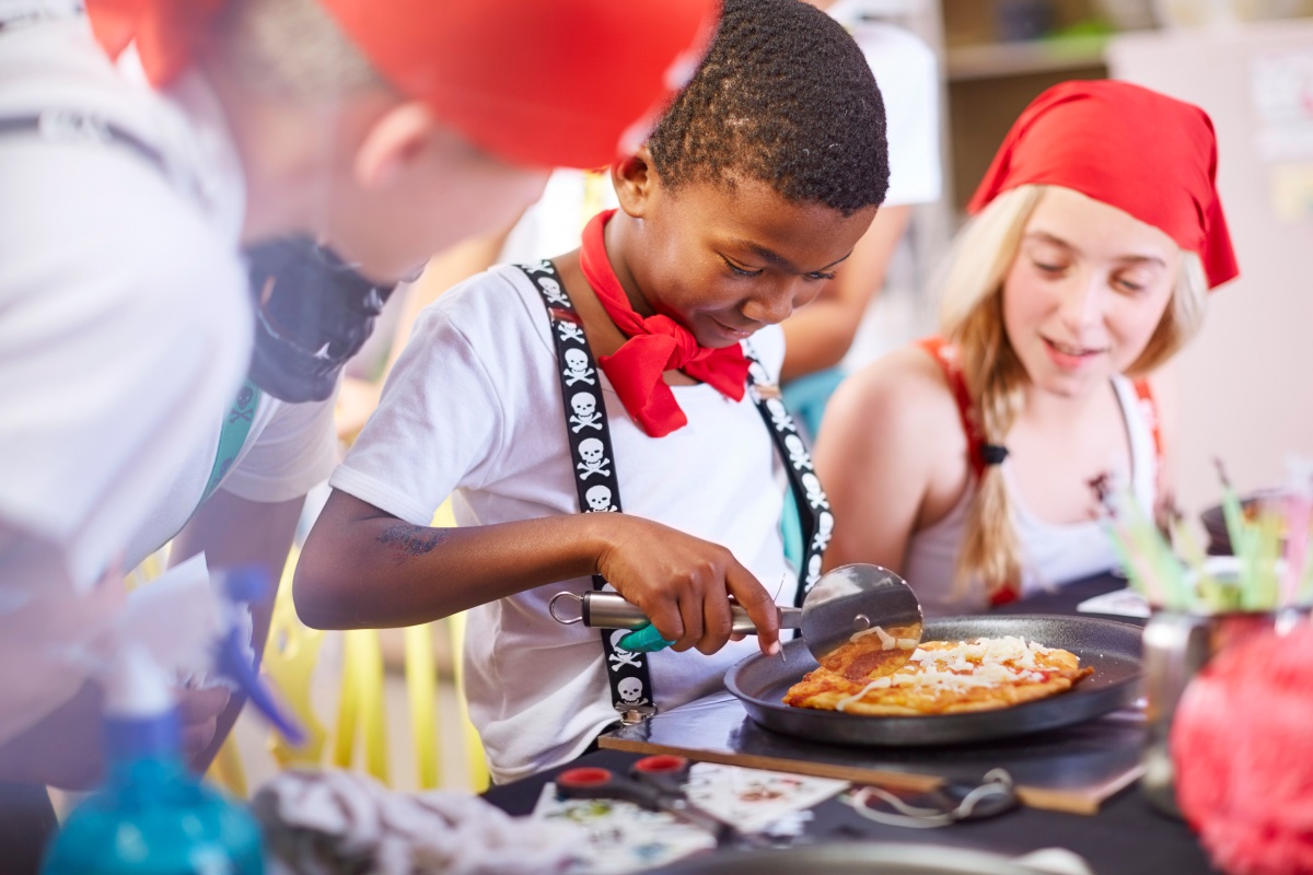 Verkleidete Kinder schneiden auf einem Kindergeburtstag eine Mini-Pizza.