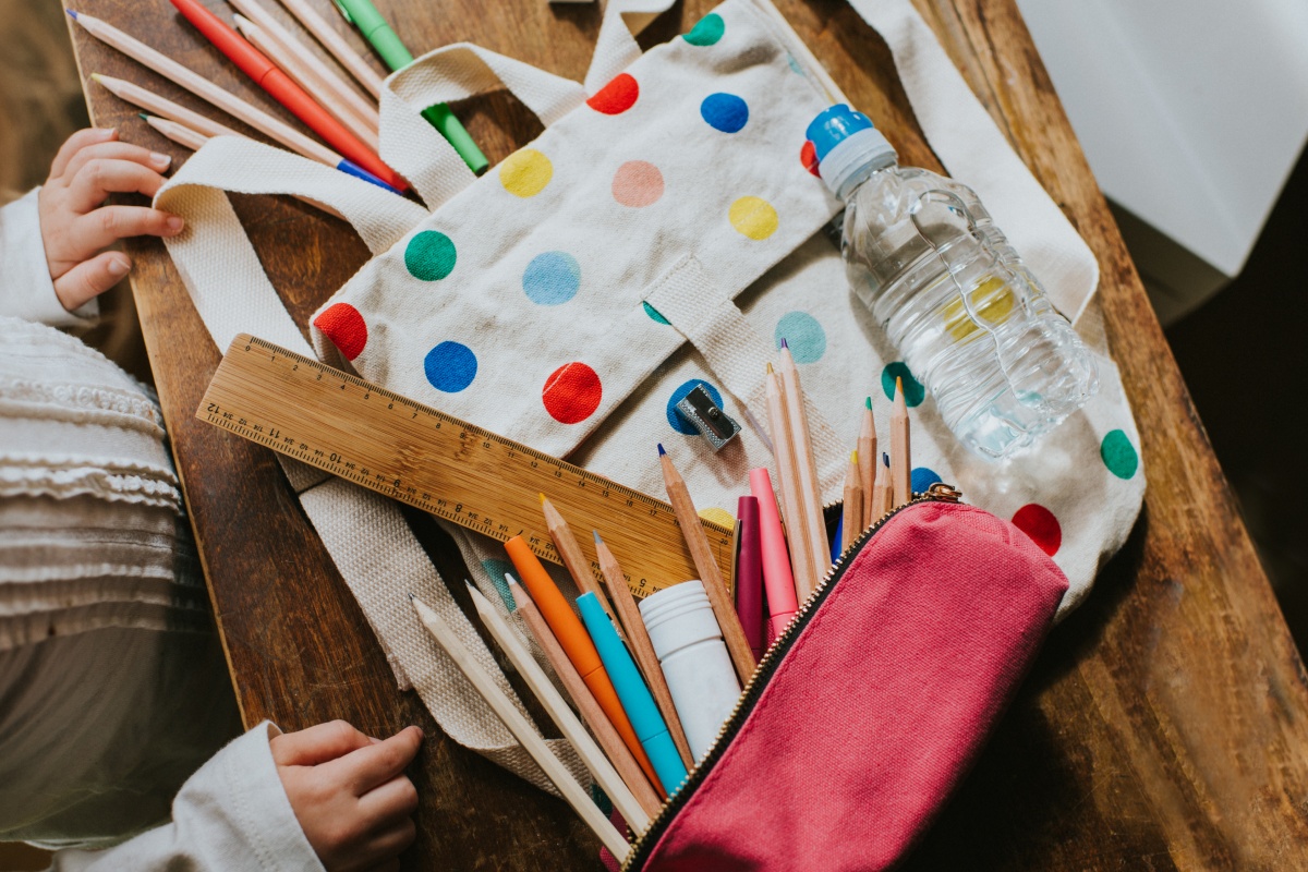 Schulutensilien wie Stifte, Lineal, Wasserflasche und gepunktete Tasche auf einem Tisch.