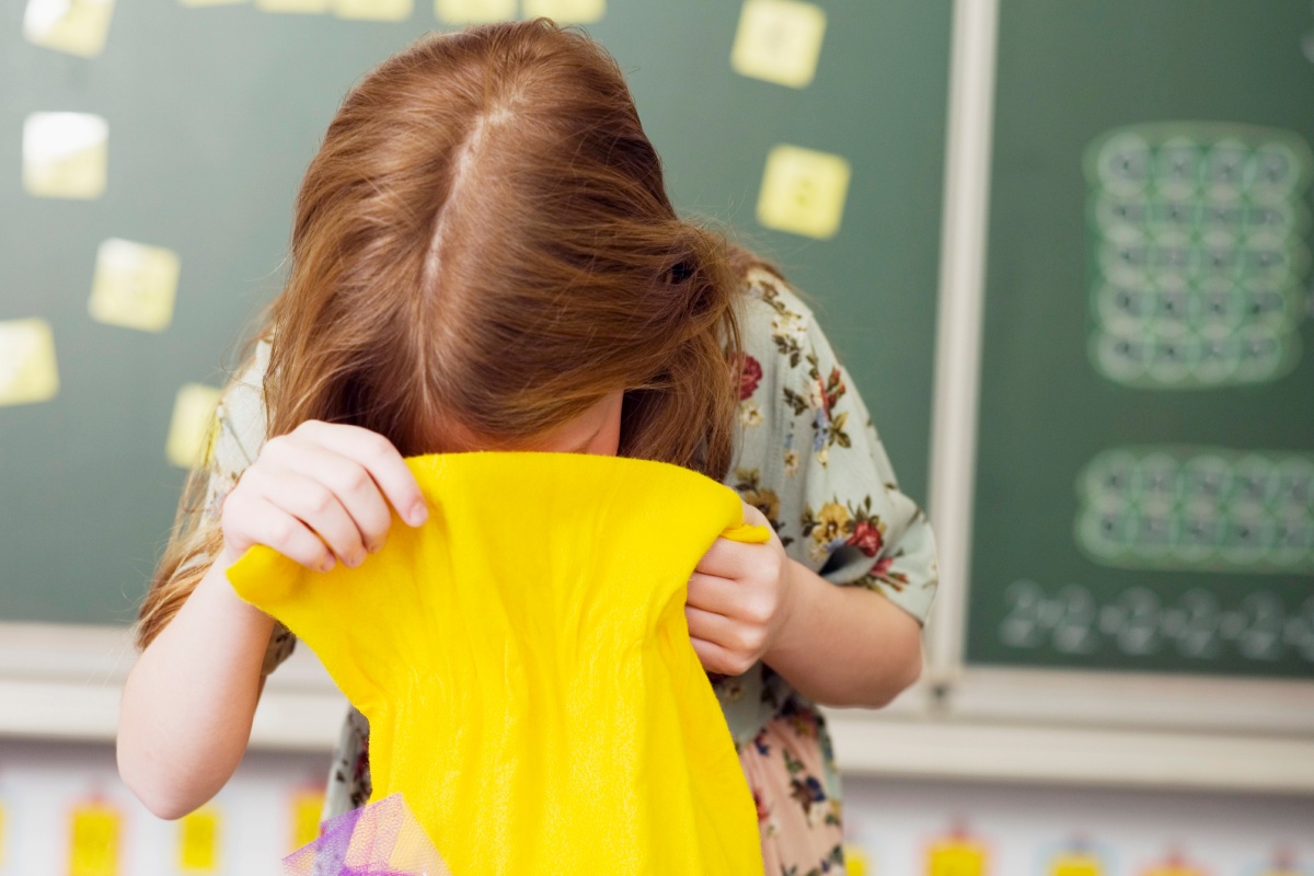 Mädchen blickt in eine gelbe Schultüte vor einer Schultafel.