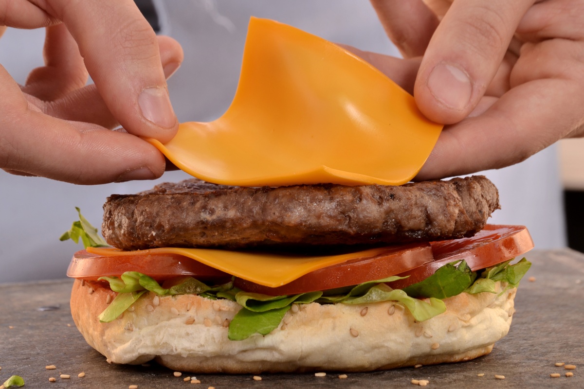 Nahaufnahme eines Burgers, der mit einer Scheibe Käse belegt wird.