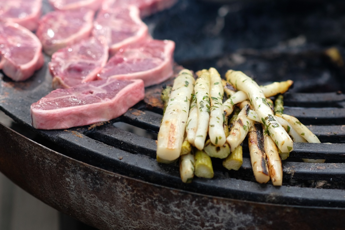 Weißer Spargel auf einem Grils, daneben noch ungegrillte Steaks.
