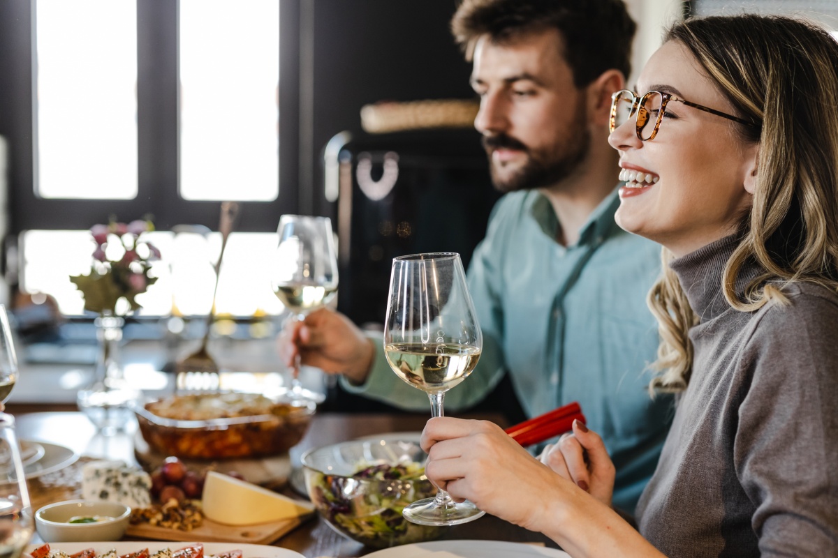 Frau und Mann beim Dinner halten Weißweingläser in den Händen. Auf dem Tische stehen Salat, Käse und Brot.