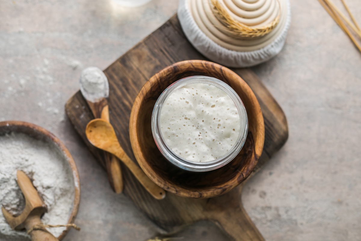 Ein Glas mit angesetztem Sauerteig, der Bläschen schlägt, auf einem Holzbrett.