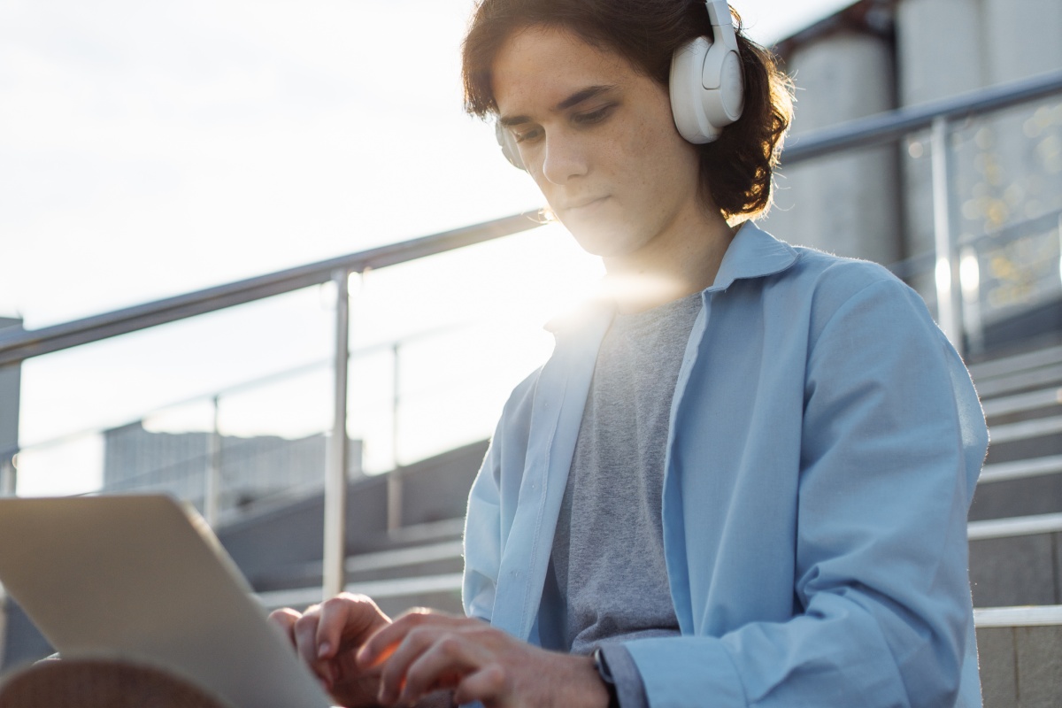 Person mit Kopfhörern shoppt oder arbeitet draußen am Laptop.