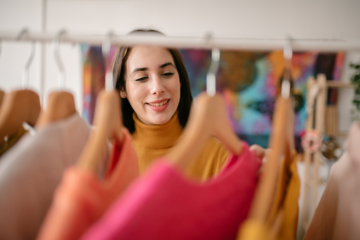 Frau schaut sich bunte Kleidung auf Kleiderbügeln an.