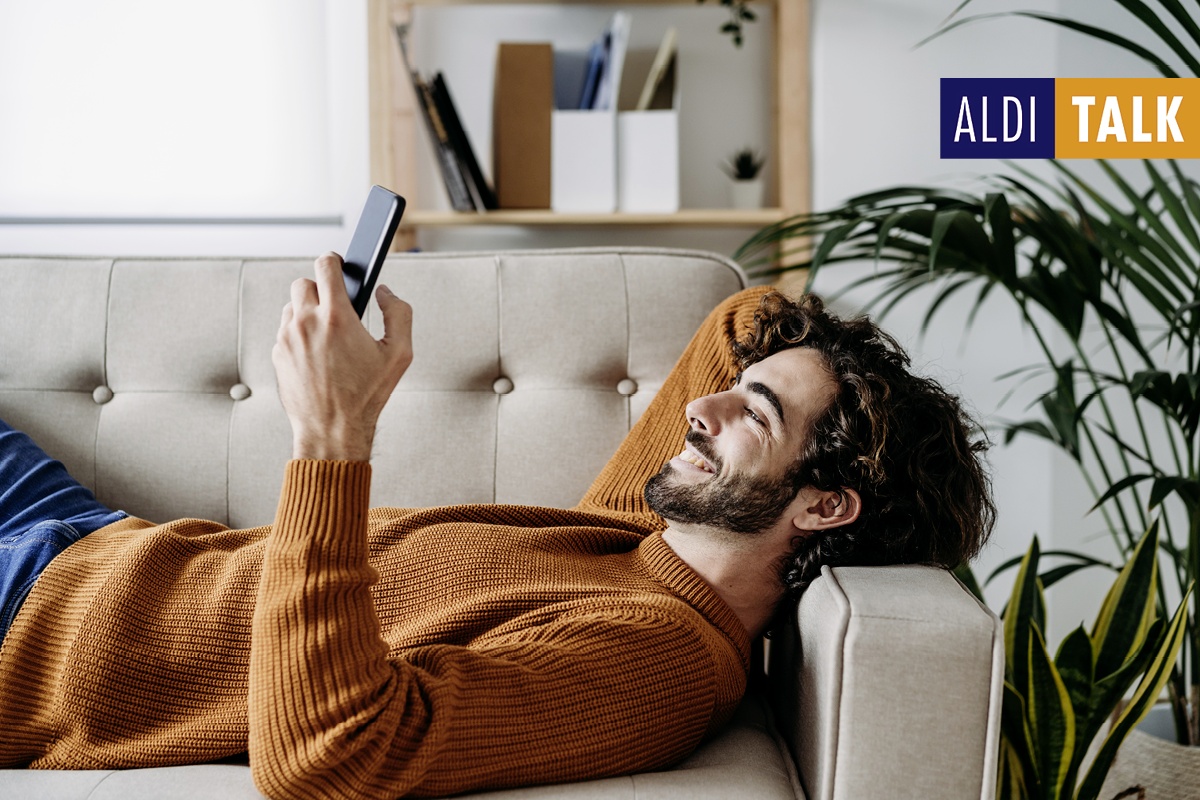 Mann entspannt auf dem Sofa und nutzt sein Smartphone.