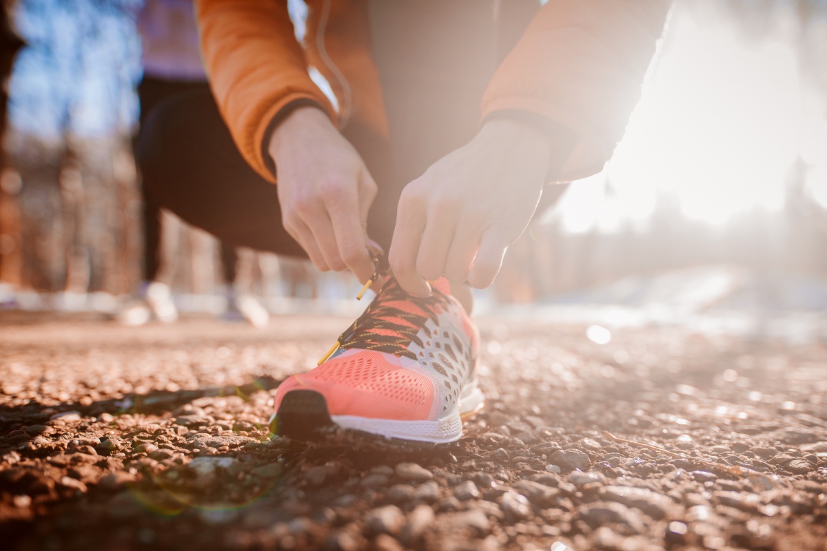 Person bindet sich orangefarbene Laufschuhe auf einem sonnigen Weg.