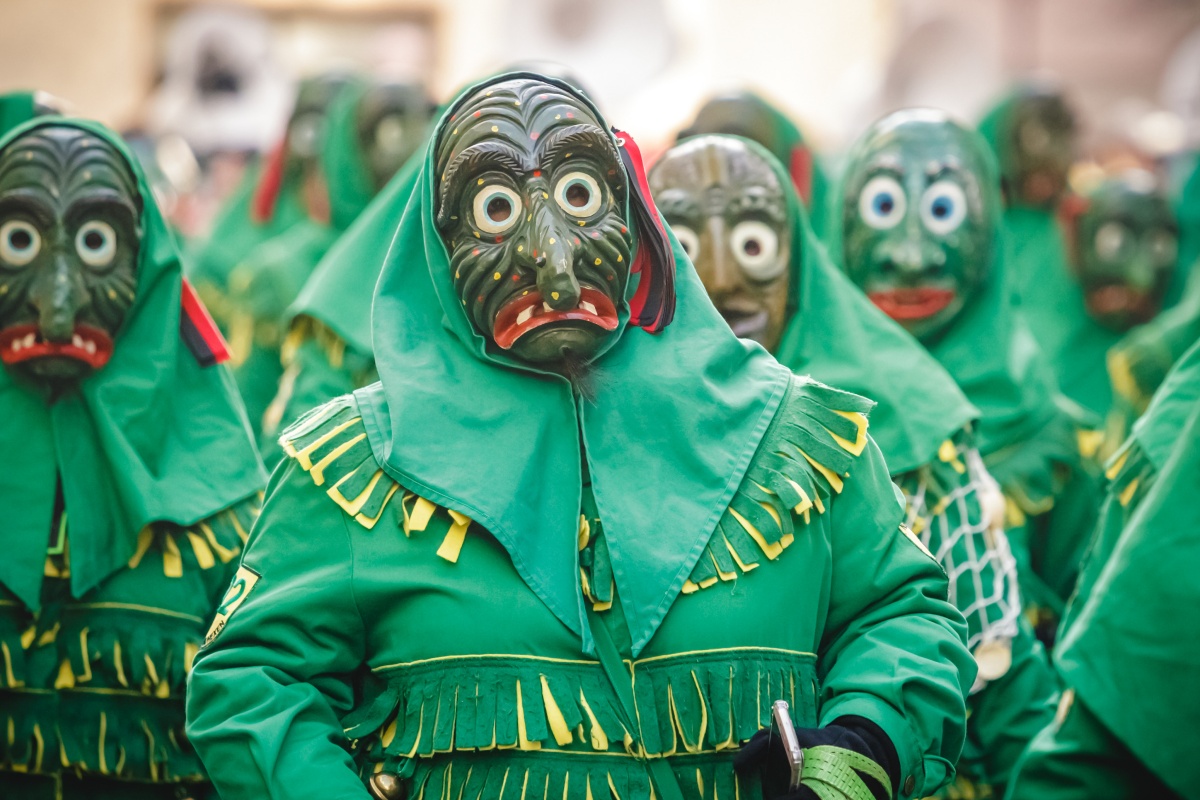 Gruppe von Personen in traditionellen, grünen geisterähnlichen Kostümen mit Holzmasken bei einem Karnevalsumzug.